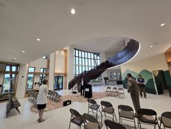 Photo of the Saratoga County Airport atrium. The atrium is a high-ceilinged room with a wall of windows in the background. A large staircase leads to the upper level.